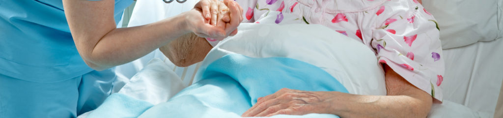 Nurse cares for a elderly patient lying in bed in hospital.